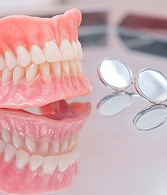 Full set of dentures on reflective surface next to dental mirror