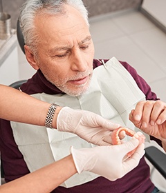 Man in dental chair reaching for dentures offered by dentist