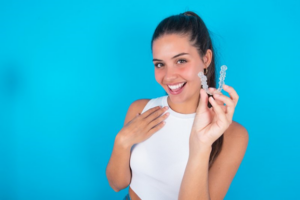 Woman smiling and holding Invisalign tray on extremely bright blue background