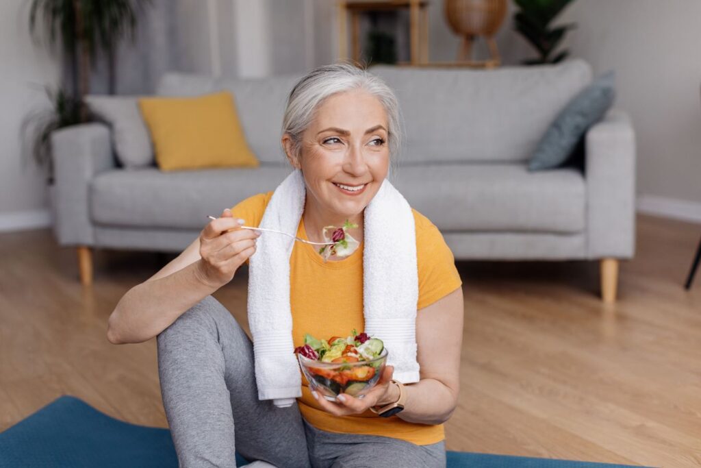 A woman sitting on a yoga mat eating a bowl of fruit.