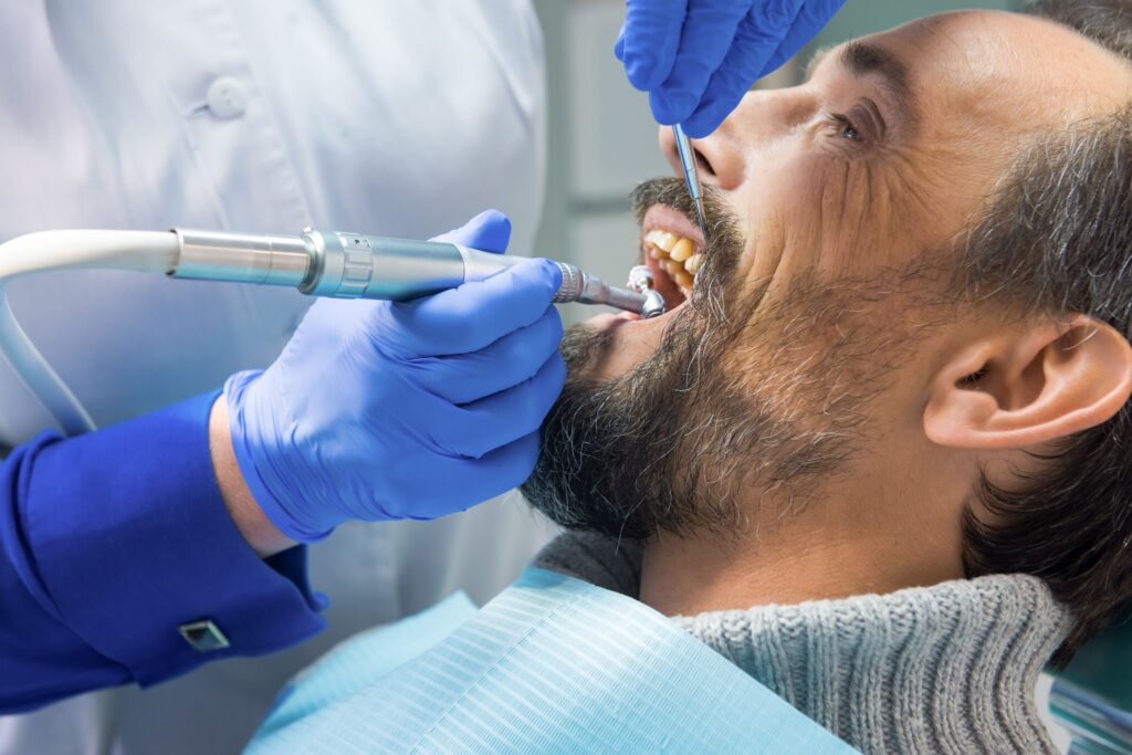 Man in gray sweater having teeth cleaned by dentist