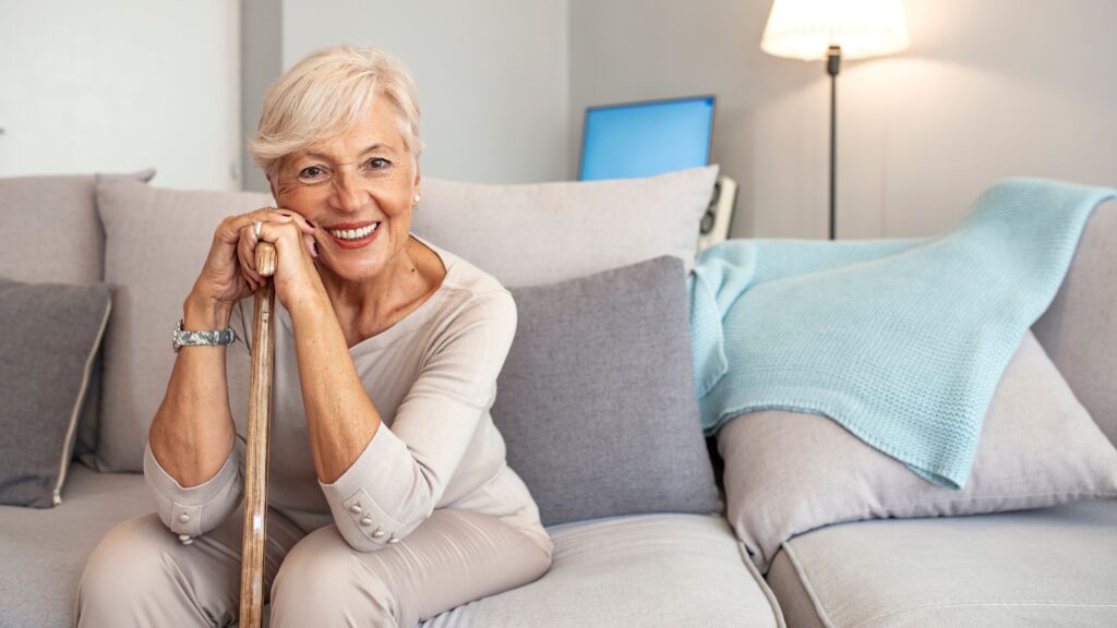 Woman in beige clothes sitting on couch leaning on cane smiling